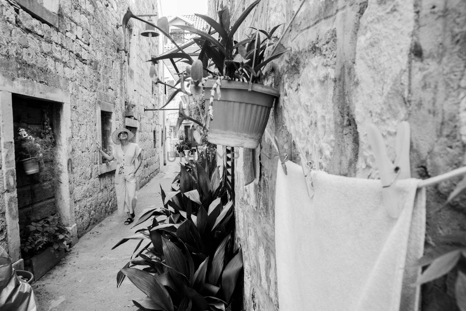 Beautiful blonde young female traveler wearing straw sun hat sightseeing and enjoying summer vacation in an old traditional costal town at Adriatic cost, Croatia. Black and white