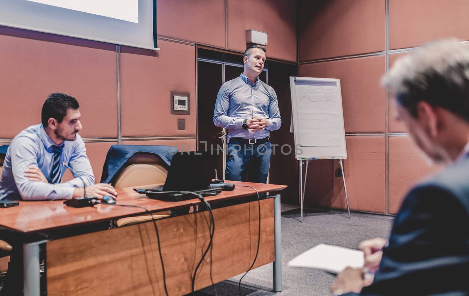 Speaker giving a talk in conference hall at business meeting event. Rear view of unrecognizable people in audience at the conference hall. Business and entrepreneurship concept.