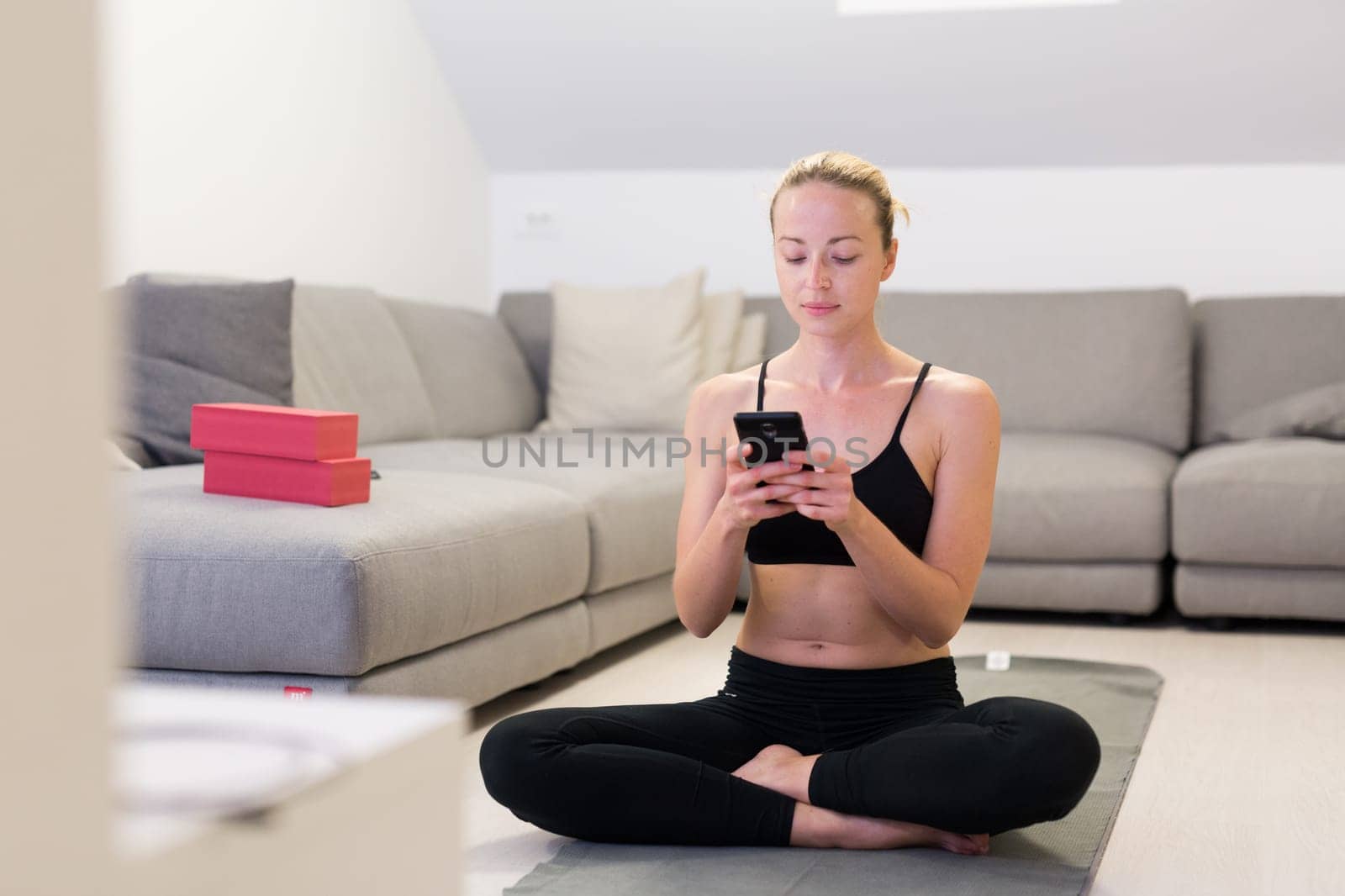 Beautiful blonde woman doing home workout indoors. Woman practice yoga at home. Fit girl using workout tutorials for healthy active lifestyle. Woman using quarantine for home workouts. Stretching