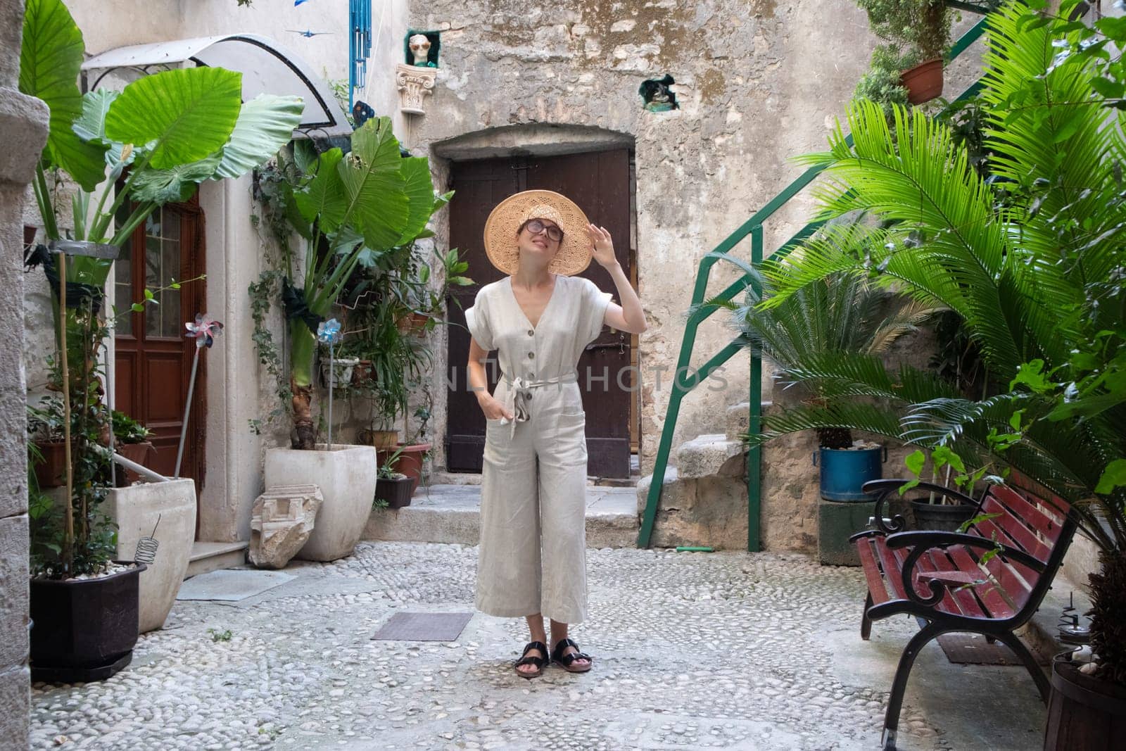 Beautiful blonde young female traveler wearing straw sun hat sightseeing and enjoying summer vacation in an old traditional costal town at Adriatic cost, Croatia.