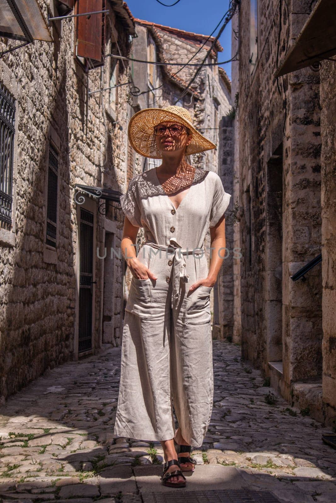 Beautiful blonde young female traveler wearing straw sun hat sightseeing and enjoying summer vacation in an old traditional costal town at Adriatic cost, Croatia.