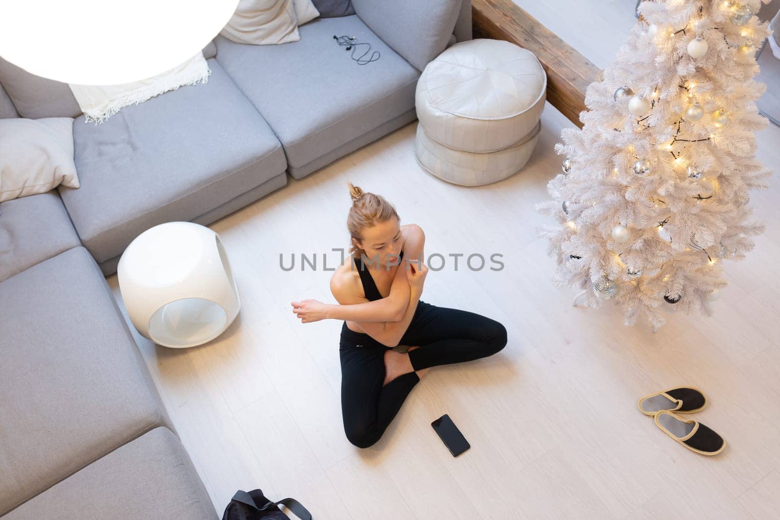 Beautiful blonde woman doing home workout indoors. Woman practice yoga at home. Fit girl using workout tutorials for healthy active lifestyle. Woman using quarantine for home workouts and stretching