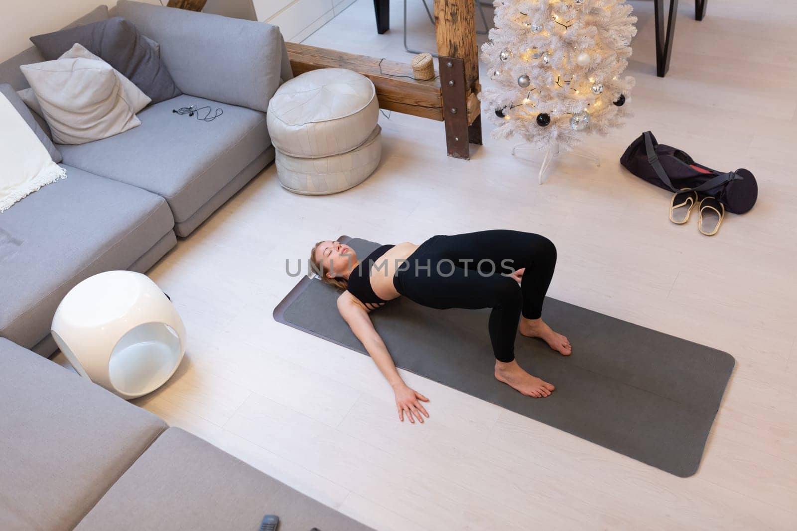 Beautiful blonde woman doing home workout indoors. Woman practice yoga at home. Fit girl using workout tutorials for healthy active lifestyle. Woman using quarantine for home workouts and stretching