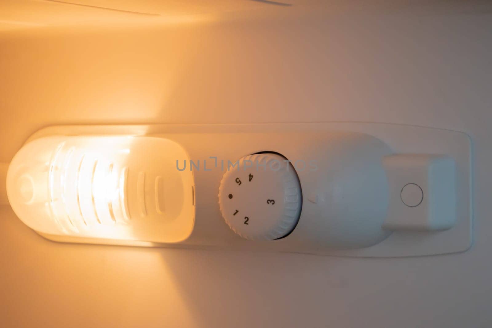Orange light inside the refrigerator close-up. A lamp that turns on when the door is open to improve vision. Household appliances concept, changing the lamp in the freezer