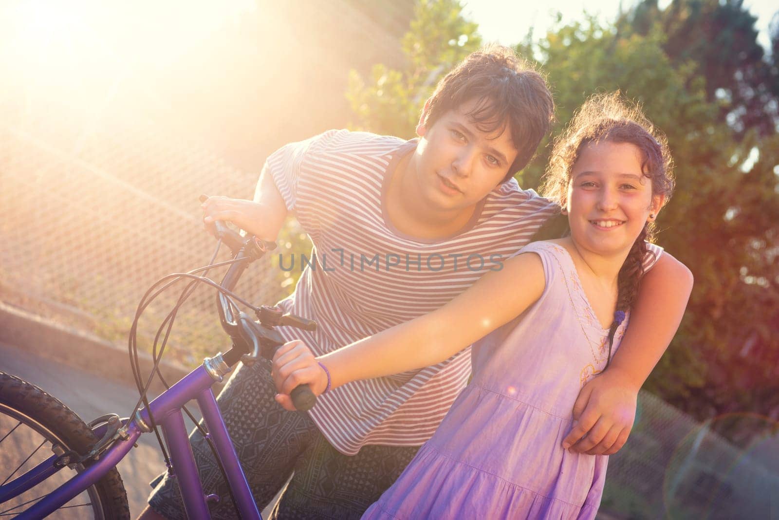 Happy young kid’s couple outdoors at sunset with bicycle