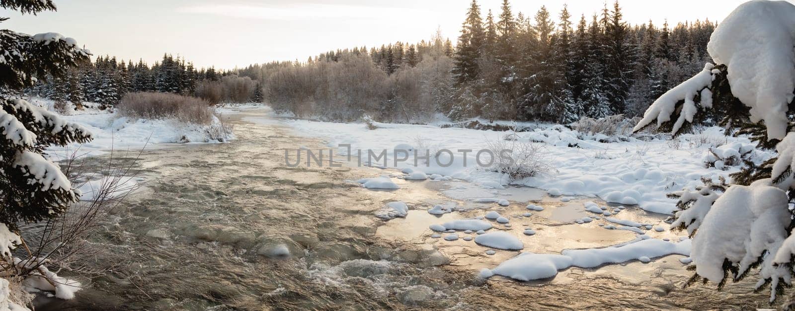 Mountain river freezing on a cold winter morning with fog rising from water. Wide angle panoramic nature scenery with trees, water and snow. Background from wilderness.