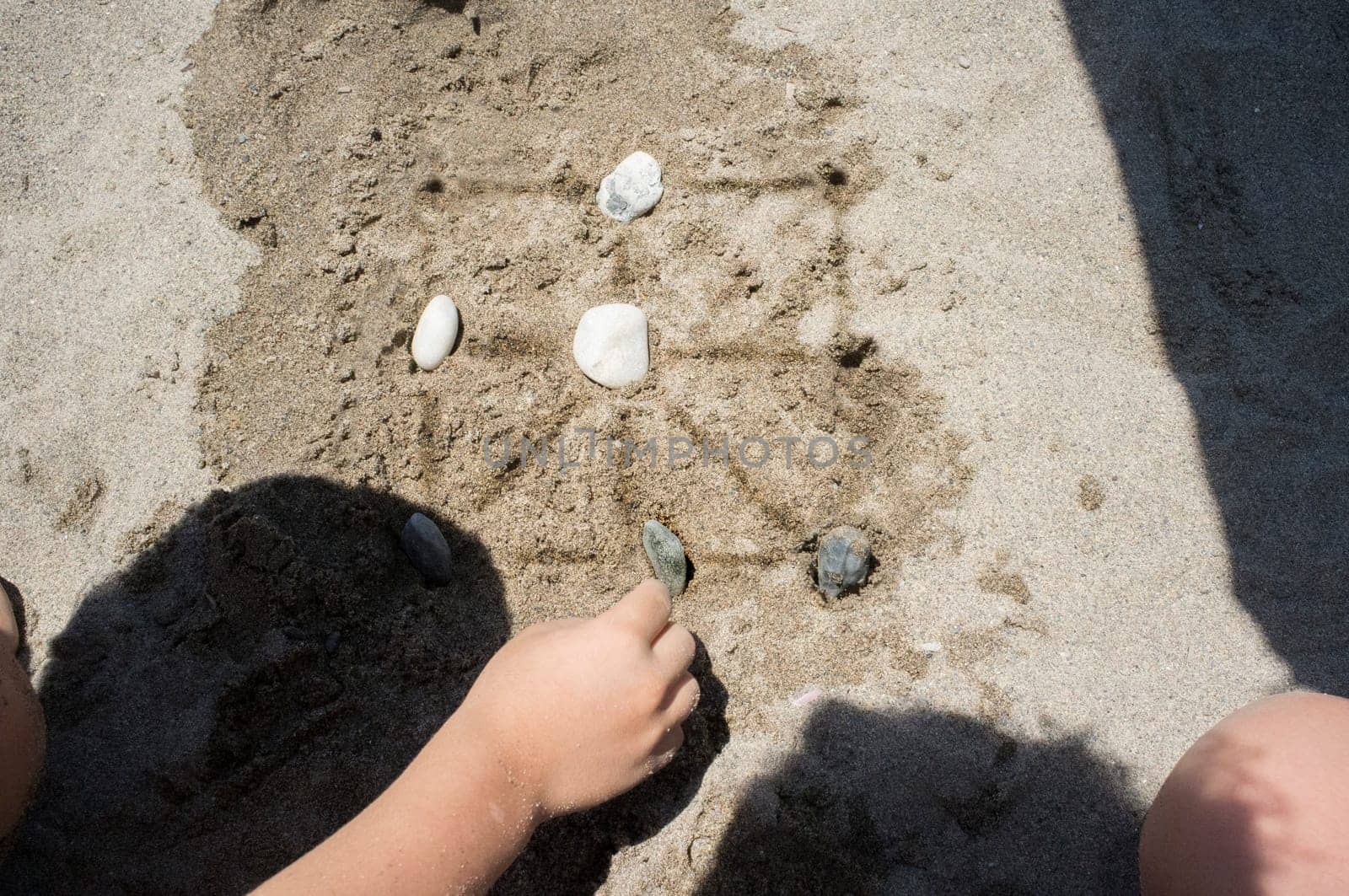 Children playing tic-tac-toe with natural board made with sand marks and beach pebbles. Overhead view