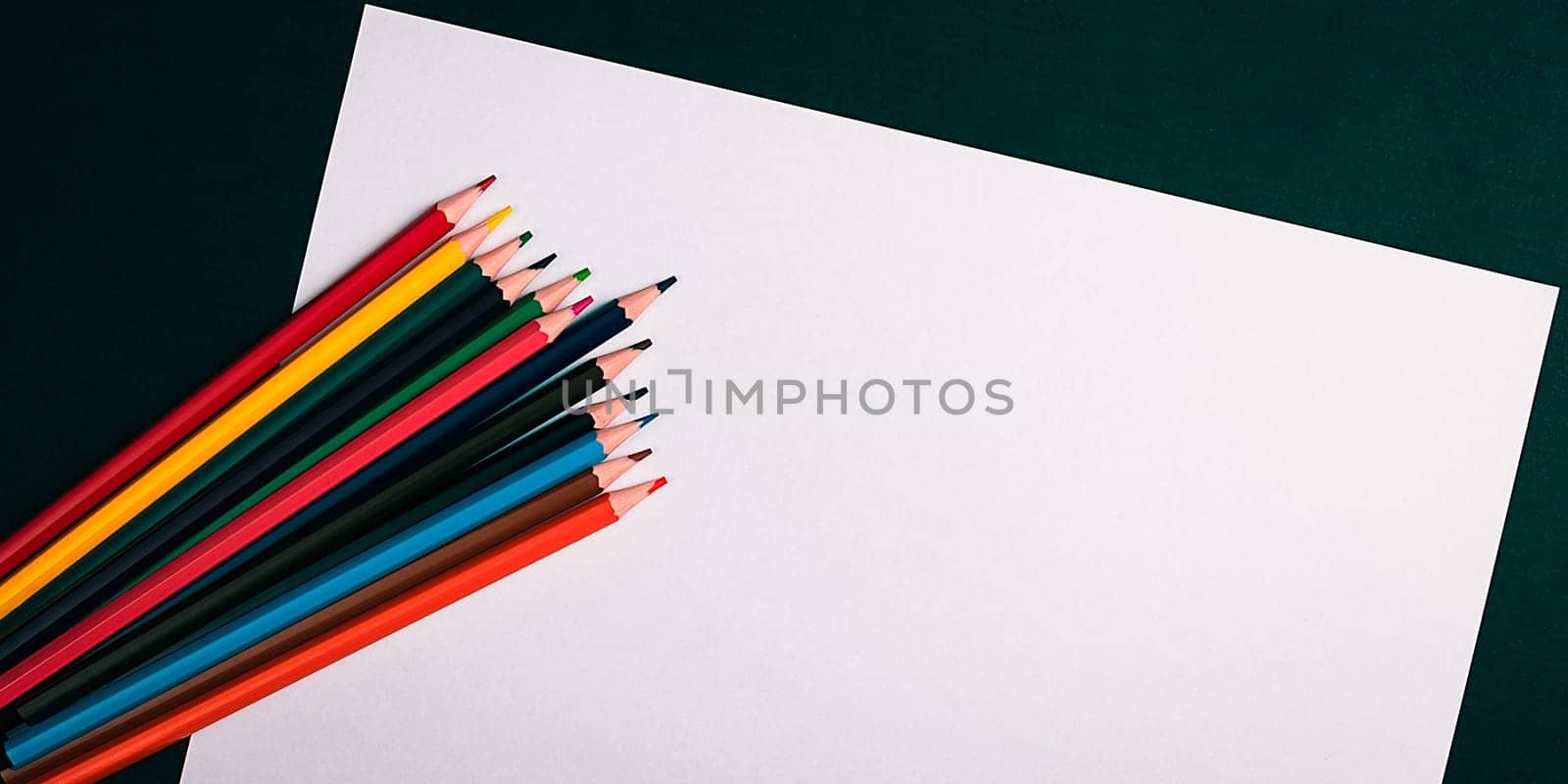 A blank white sheet and colored pencils for drawing on a plain textured background with space for copying and lettering. Layout, mockup free space.
