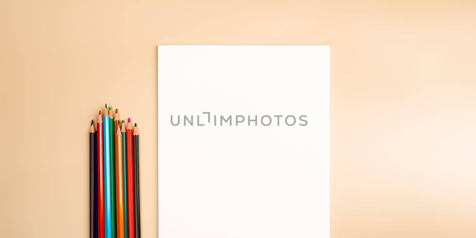 A blank white sheet and colored pencils for drawing on a plain textured background with space for copying and lettering. Layout, mockup free space.