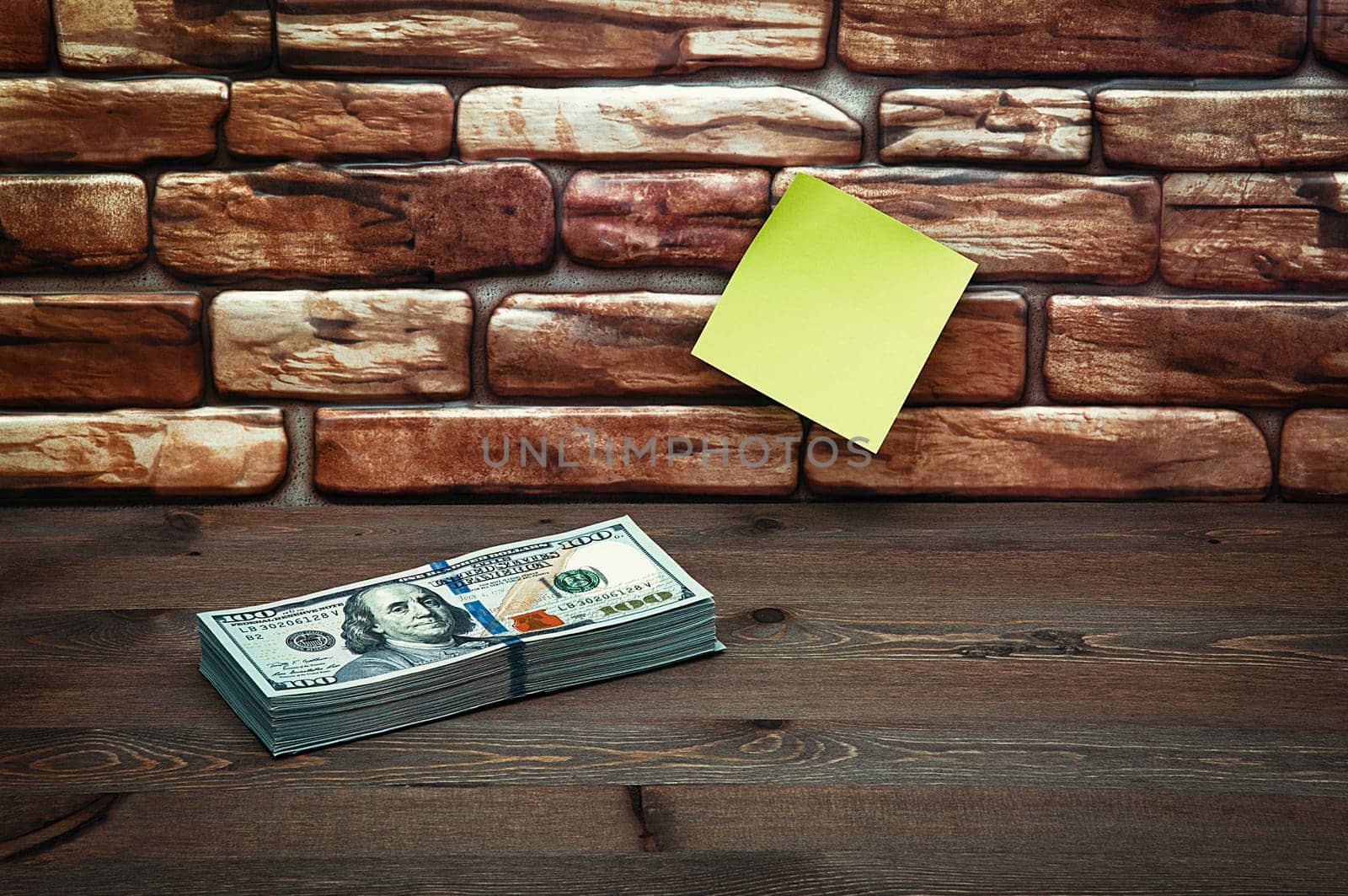 Dollars in one-hundred-dollar bills are stacked on a table near the brick wall. Dollars in a big pile. US dollars. On the brown brick wall there is a place for an inscription, a logo. Color style. Layout, template, mockup.