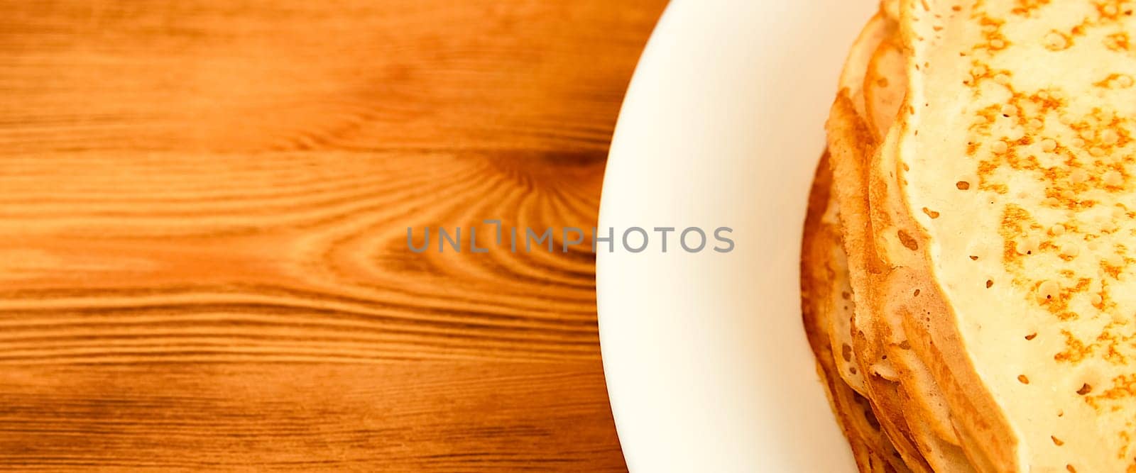 Pancakes on a plate on a wooden table. A large stack of fresh pancakes. Delicious healthy fresh pancakes. Place for advertising, logo, lettering, layout, mockup.