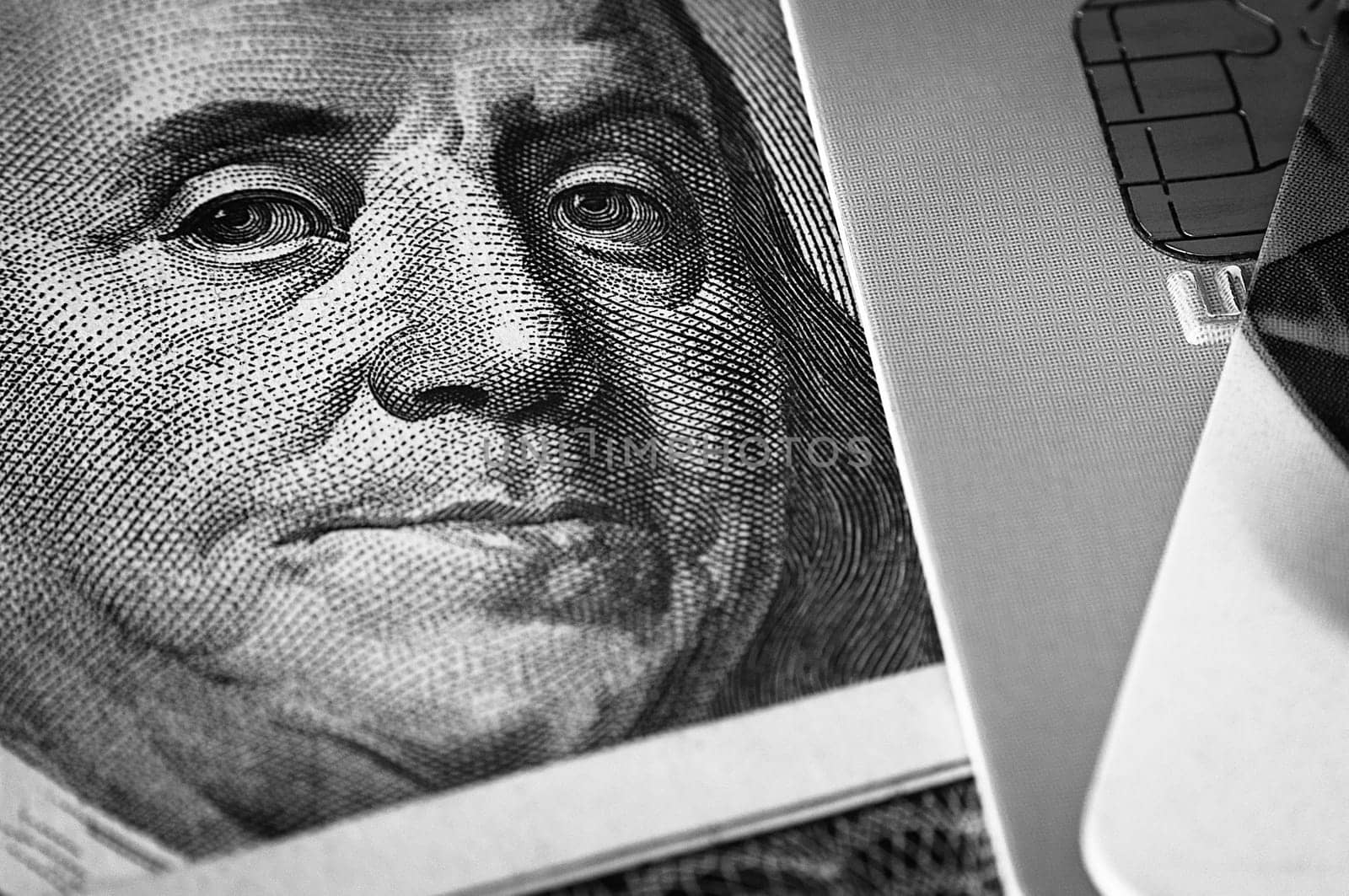 Benjamin Franklin's face on a hundred-dollar bill next to a credit card. Close-up. A hundred-dollar American bill with the eyes of Benjamin Franklin. Black and white style. Layout, template, layout.