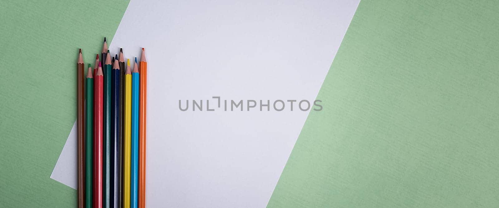 A blank white sheet and colored pencils for drawing on a plain textured background with space for copying and lettering. Layout, mockup free space.