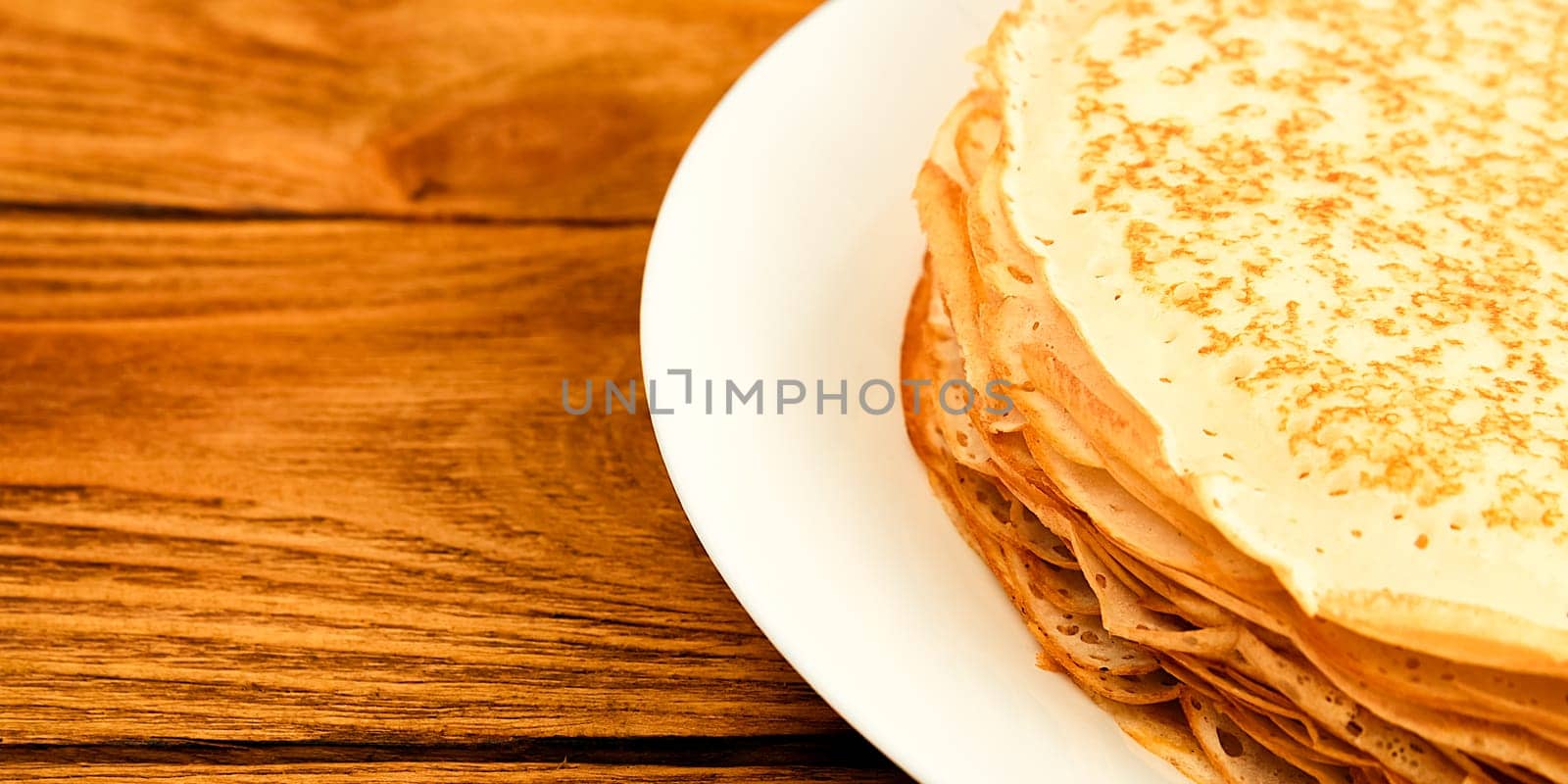 Pancakes on a plate on a wooden table. A large stack of fresh pancakes. Delicious healthy fresh pancakes. Place for advertising, logo, lettering, layout, mockup.