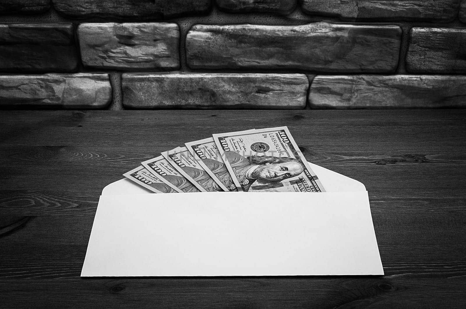 Dollars in one-hundred-dollar bills are spread out in an envelope on a table near the brick wall. Dollars fanned out. US dollars. On the envelope there is a place for an inscription, a logo. Black and white style. Layout, template, mockup.