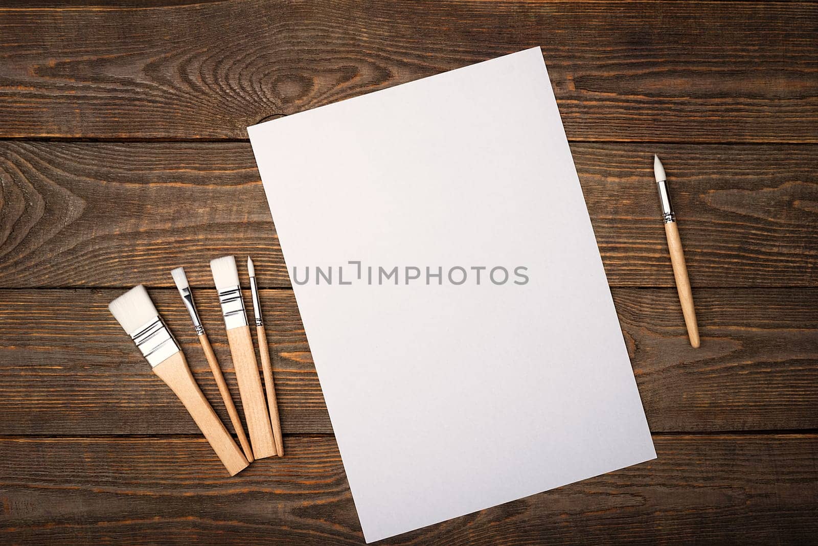 A clean white sheet and brushes on a textured background with space to copy. Layout, mockup space for text and drawing.