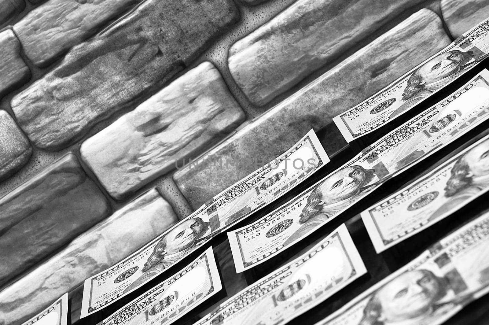 Dollars in one-hundred-dollar bills are spread out on a table near the brick wall. The dollars are arranged in a row. US dollars. On the brown brick wall there is a place for an inscription, a logo. Black and white style. Layout, template, mockup.