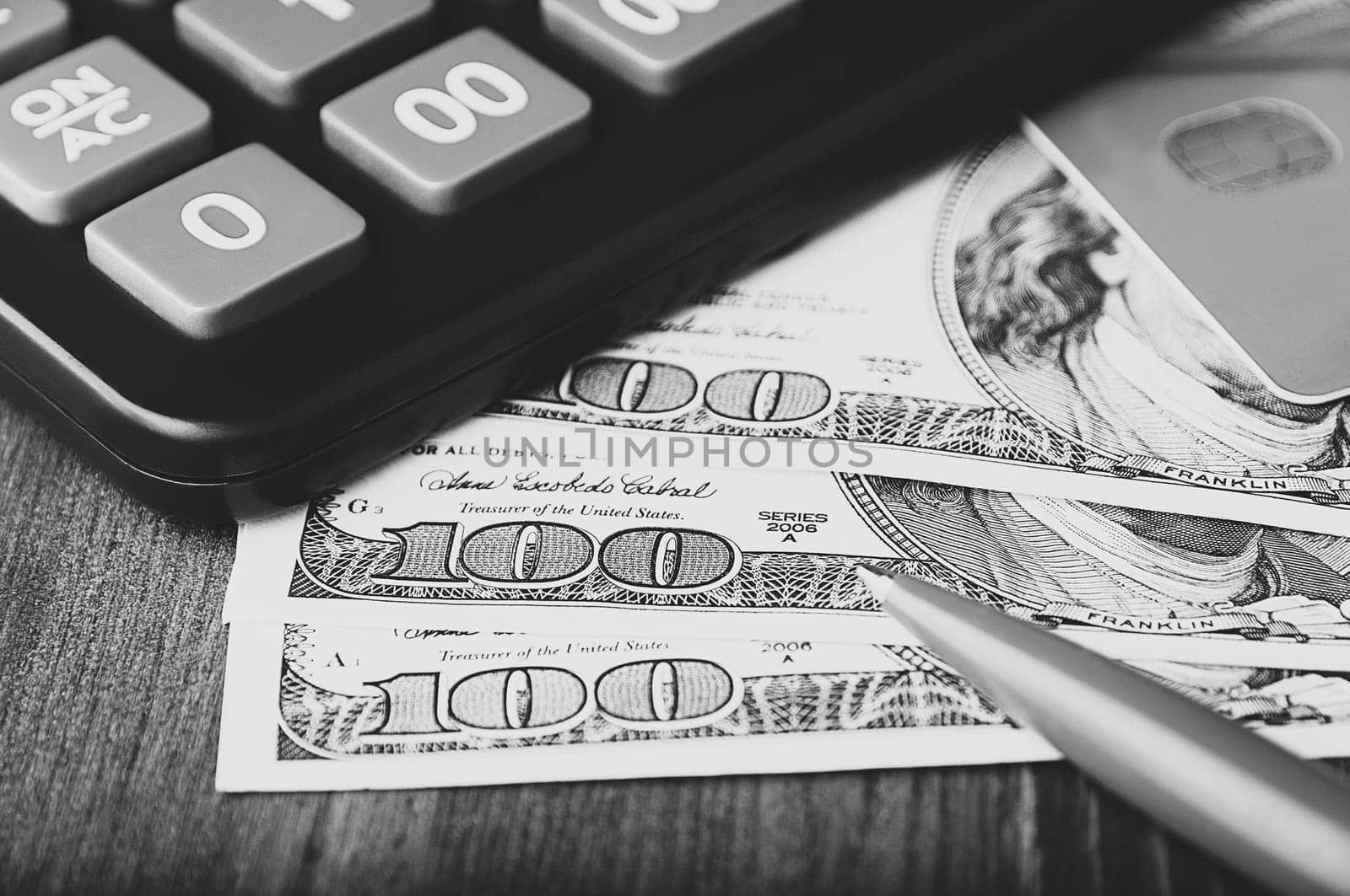 Dollars in one-hundred-dollar bills are spread out on the table next to a calculator, a credit card, and a pen. One-hundred-dollar bills. US dollars. Black and white style. Layout, template, mockup.
