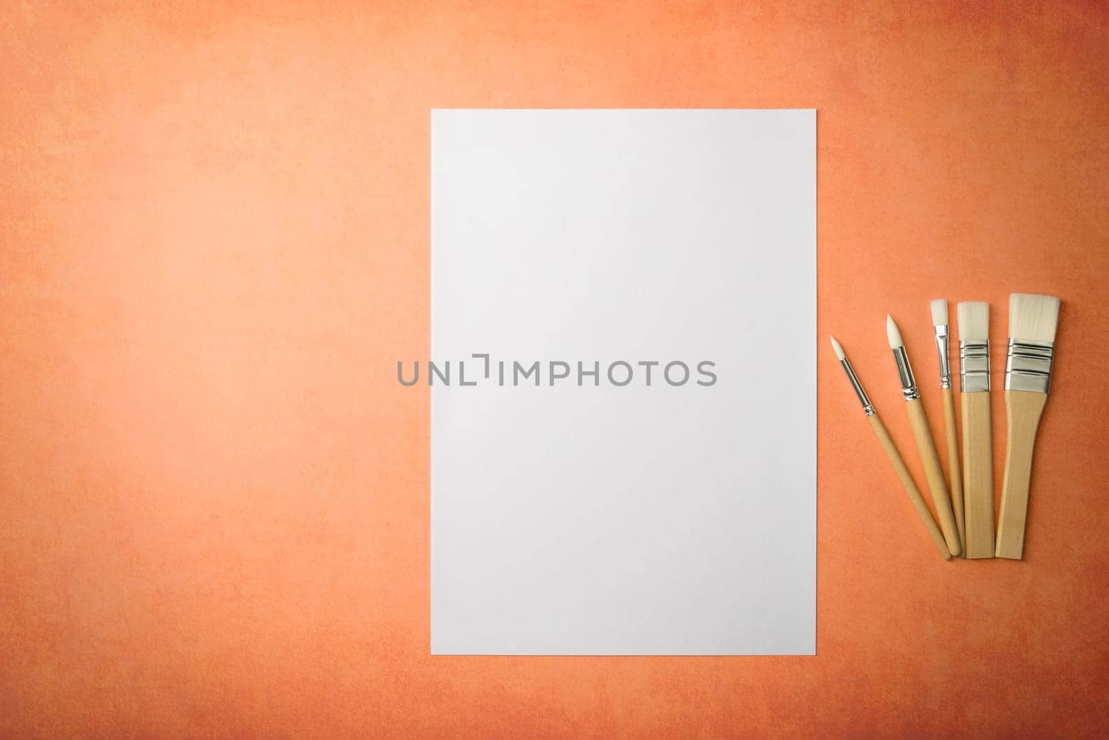 A clean white sheet and brushes on a textured background with space to copy. Layout, mockup space for text and drawing.