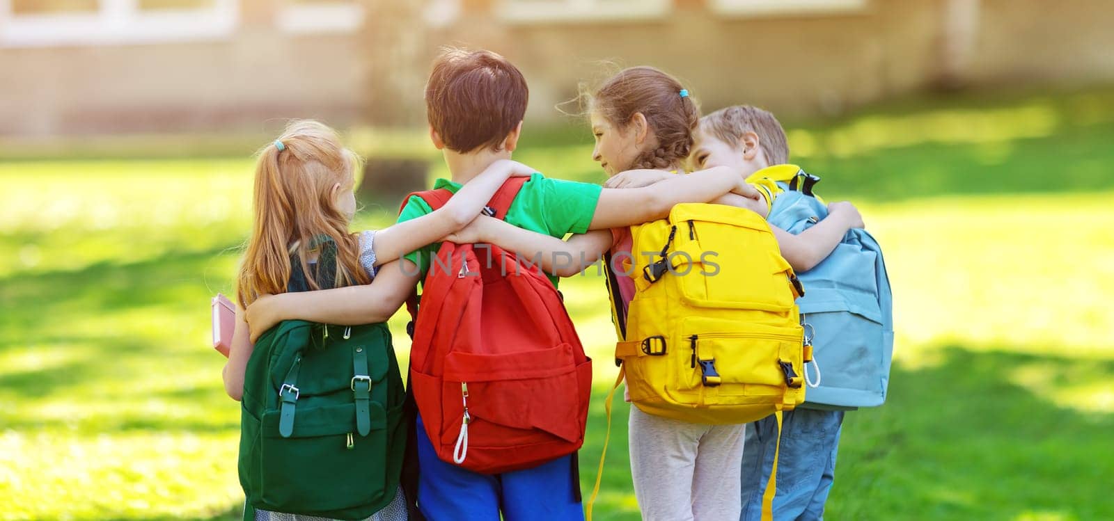 Group of children with rucksacks standing in the park near the school. Concept of elementary studying and friendship.