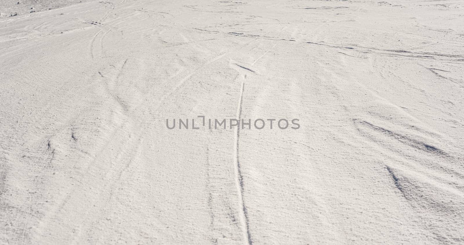Slope covered with crystalline snow, few trails from ski visible.