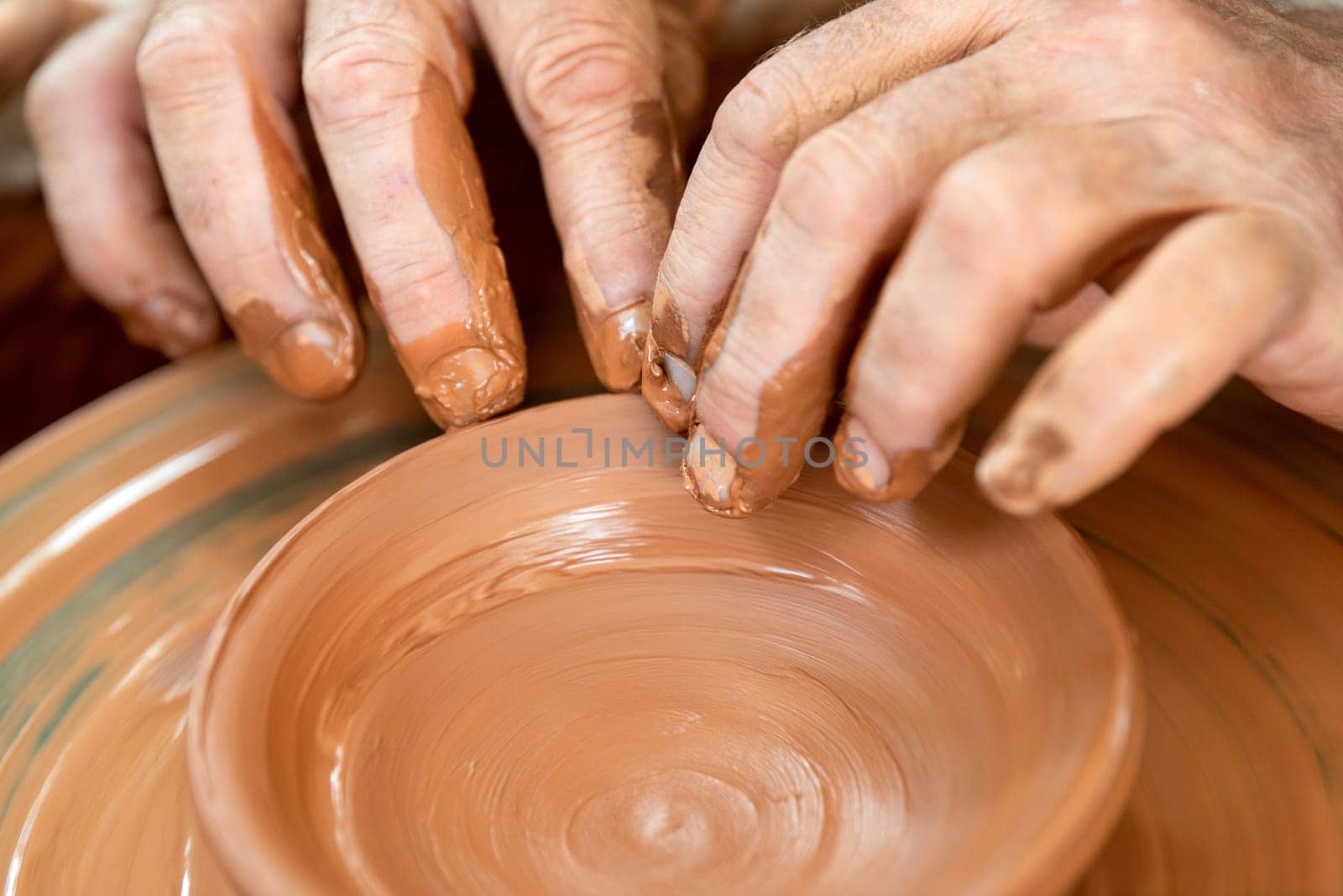 Hands of the potter. The potter makes pottery dishes on potter's wheel. The sculptor in workshop makes clay product closeup