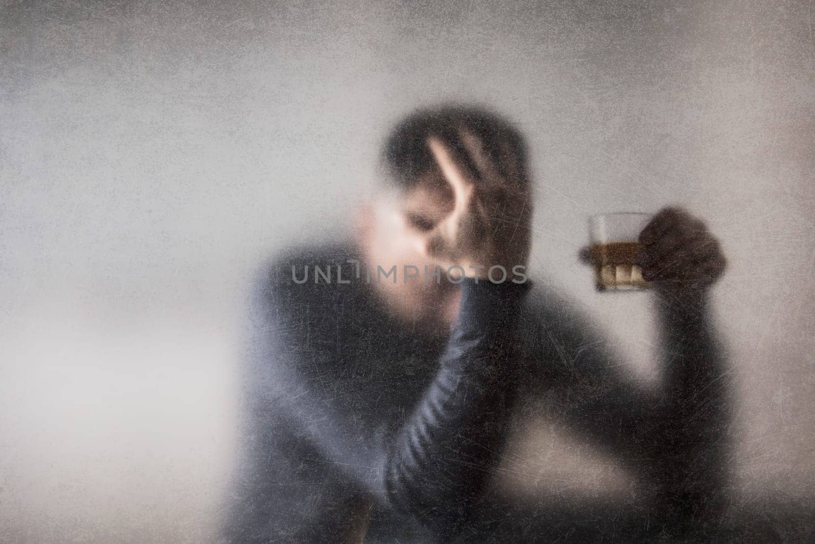 Man with a glass of whiskey behind a dusty scratched glass. Alcoholism concept.