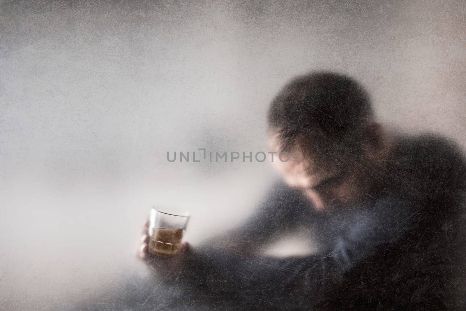 Man with a glass of whiskey behind a dusty scratched glass. Alcoholism concept.