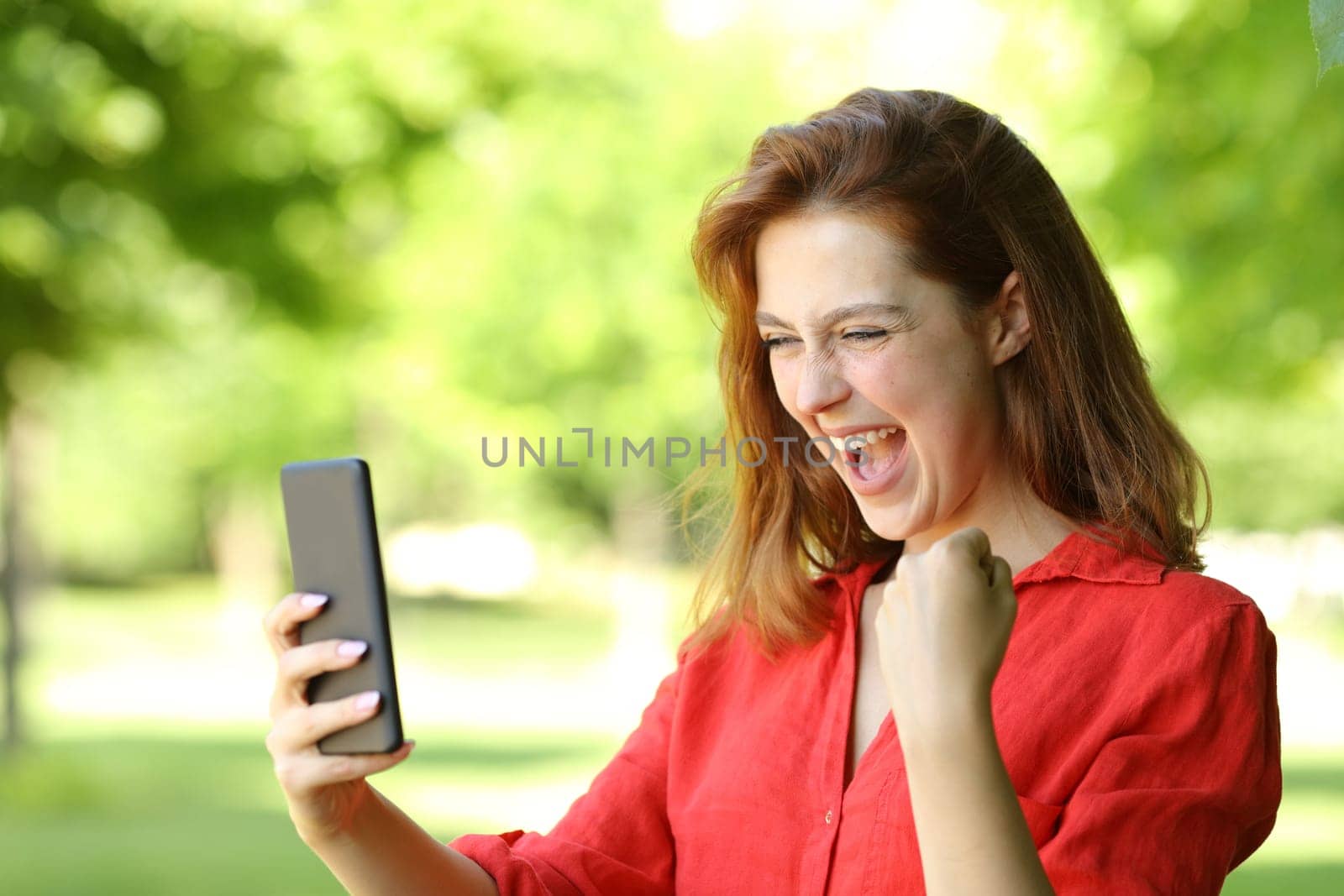 Excited woman in red celebrating checking phone