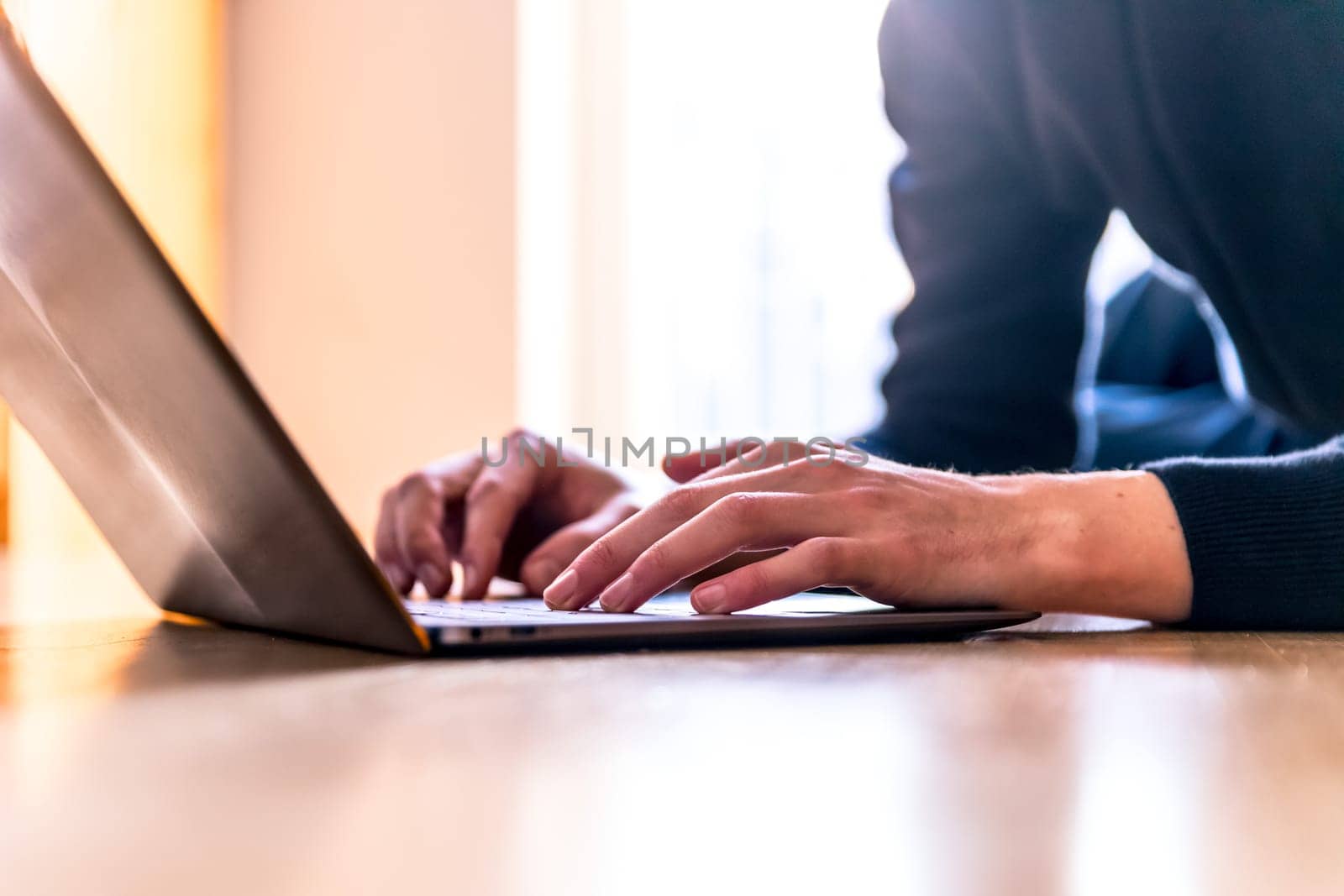Young man with a laptop is working on the wooden floor, light comes in from the window