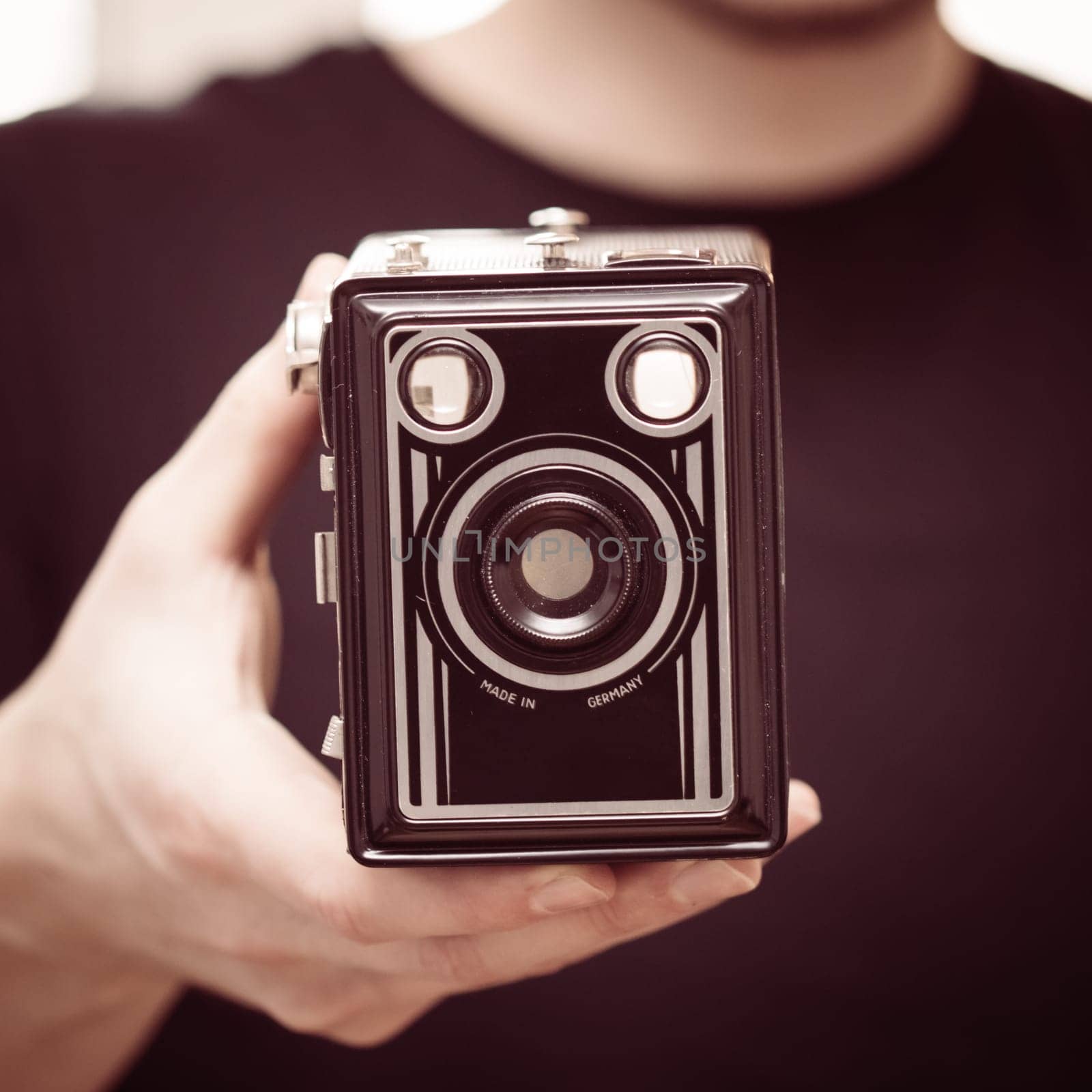 Young man in black shirt is taking a picture with a black german vintage camera