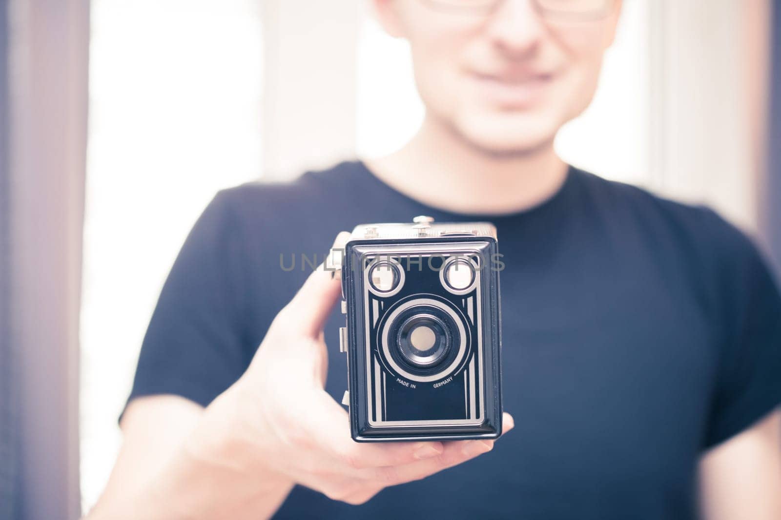 Young man in black shirt is taking a picture with a black german vintage camera