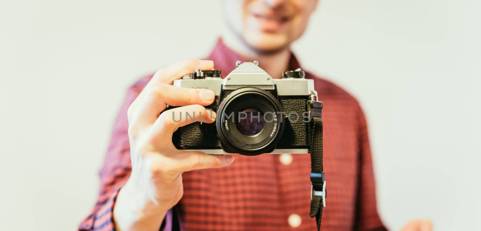 Young man in red-blue checked shirt is taking a picture with an vintage camera, retro style