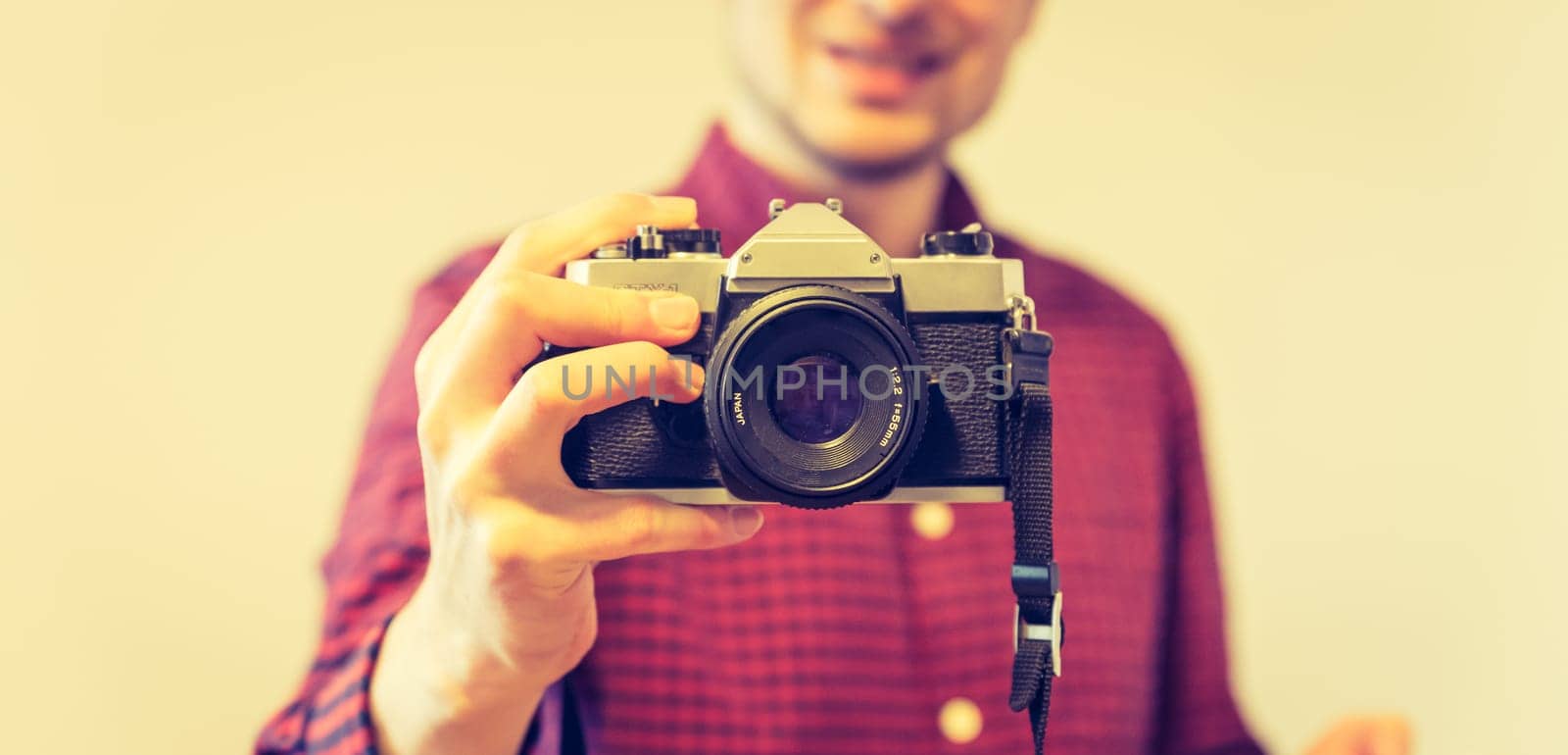Young man in red-blue checked shirt is taking a picture with an vintage camera, retro style