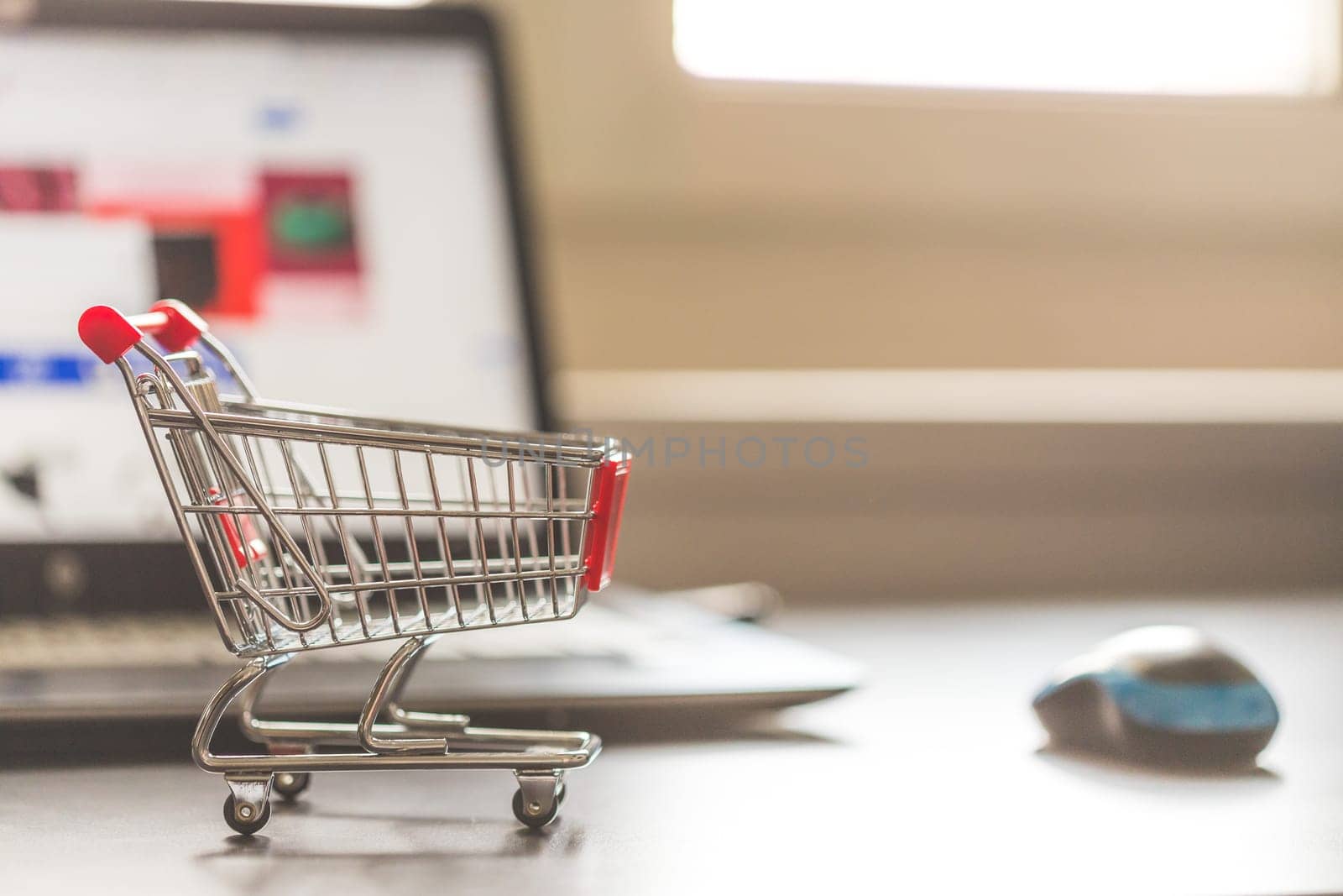 Online-Shopping concept: Miniature shopping cart, laptop and mouse in the blurry background