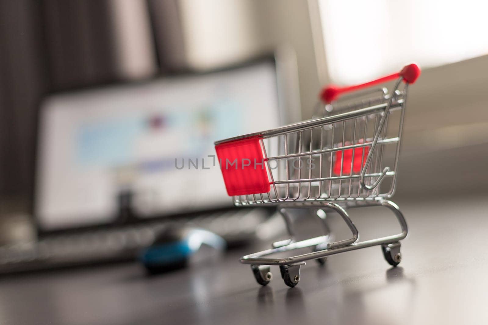 Online-Shopping concept: Miniature shopping cart, laptop and mouse in the blurry background