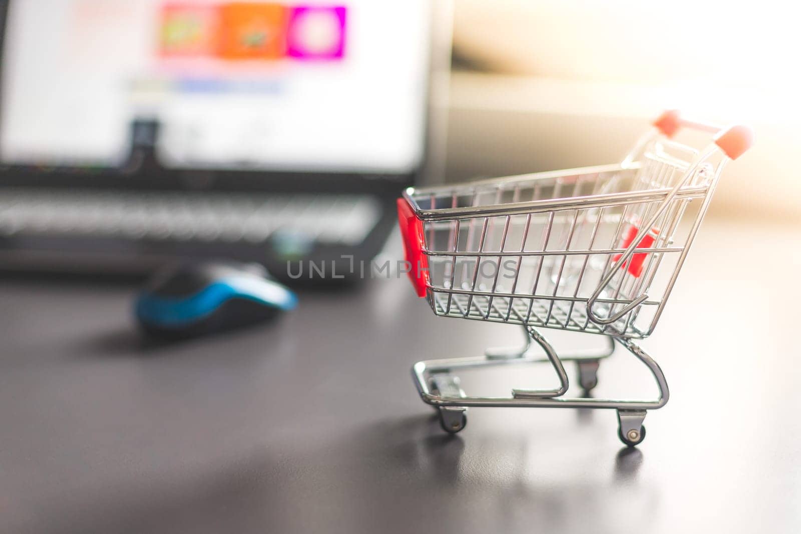 Online-Shopping concept: Miniature shopping cart, laptop and mouse in the blurry background
