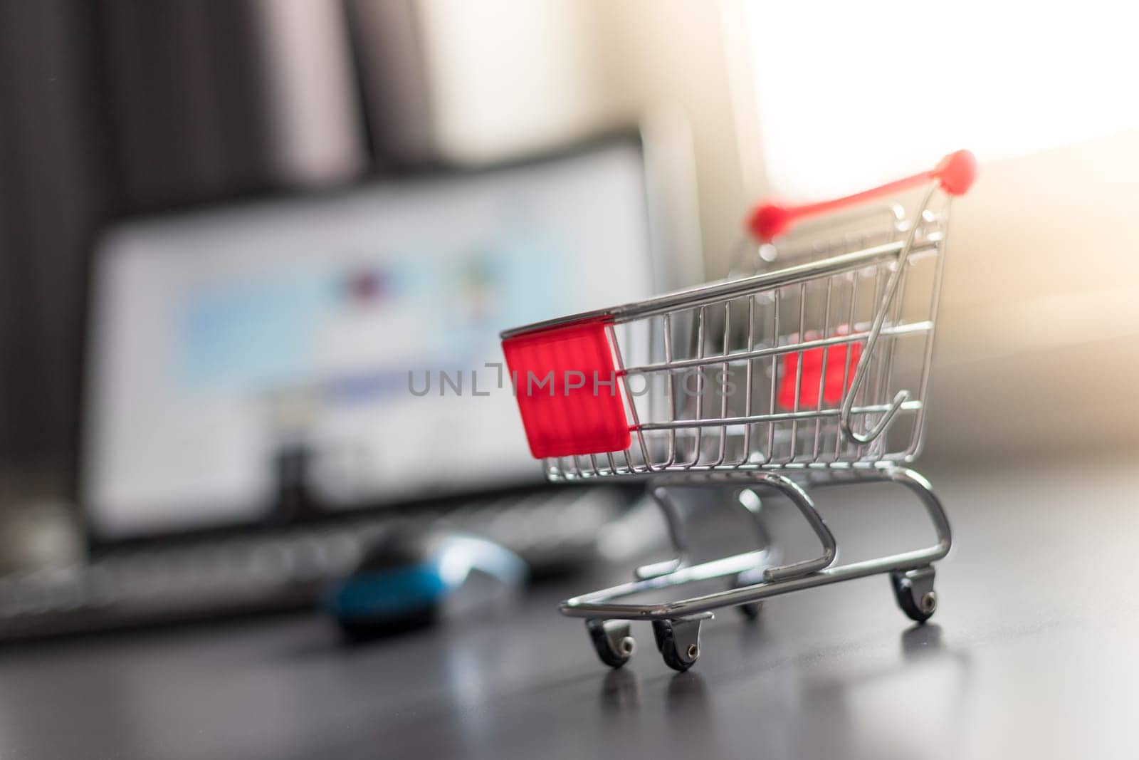 Online-Shopping concept: Miniature shopping cart, laptop and mouse in the blurry background
