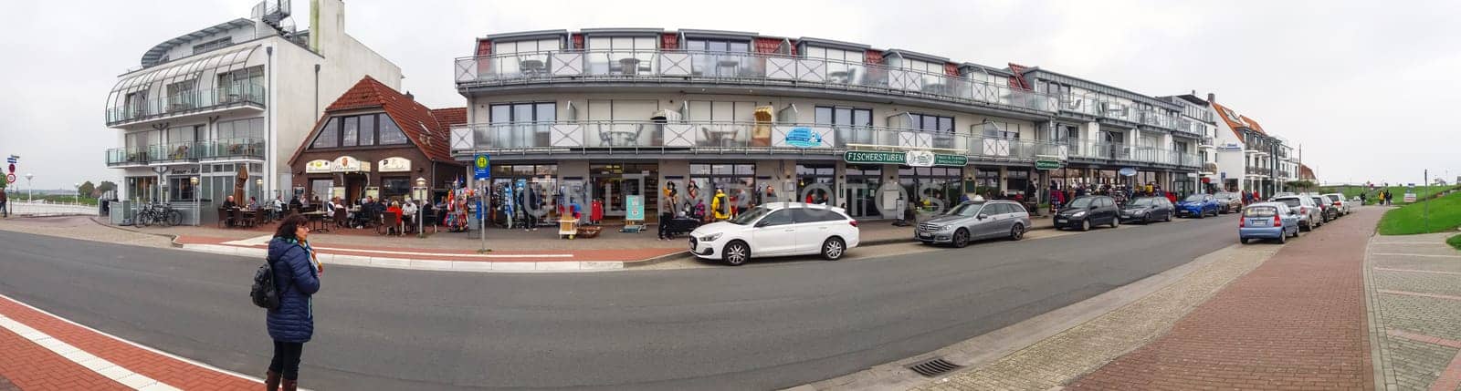 Bensersiel, Germany - May 12, 2021: Panorama view of the well-frequented row of shops in Bensersiel with overcast skies during the corona pandemic.
