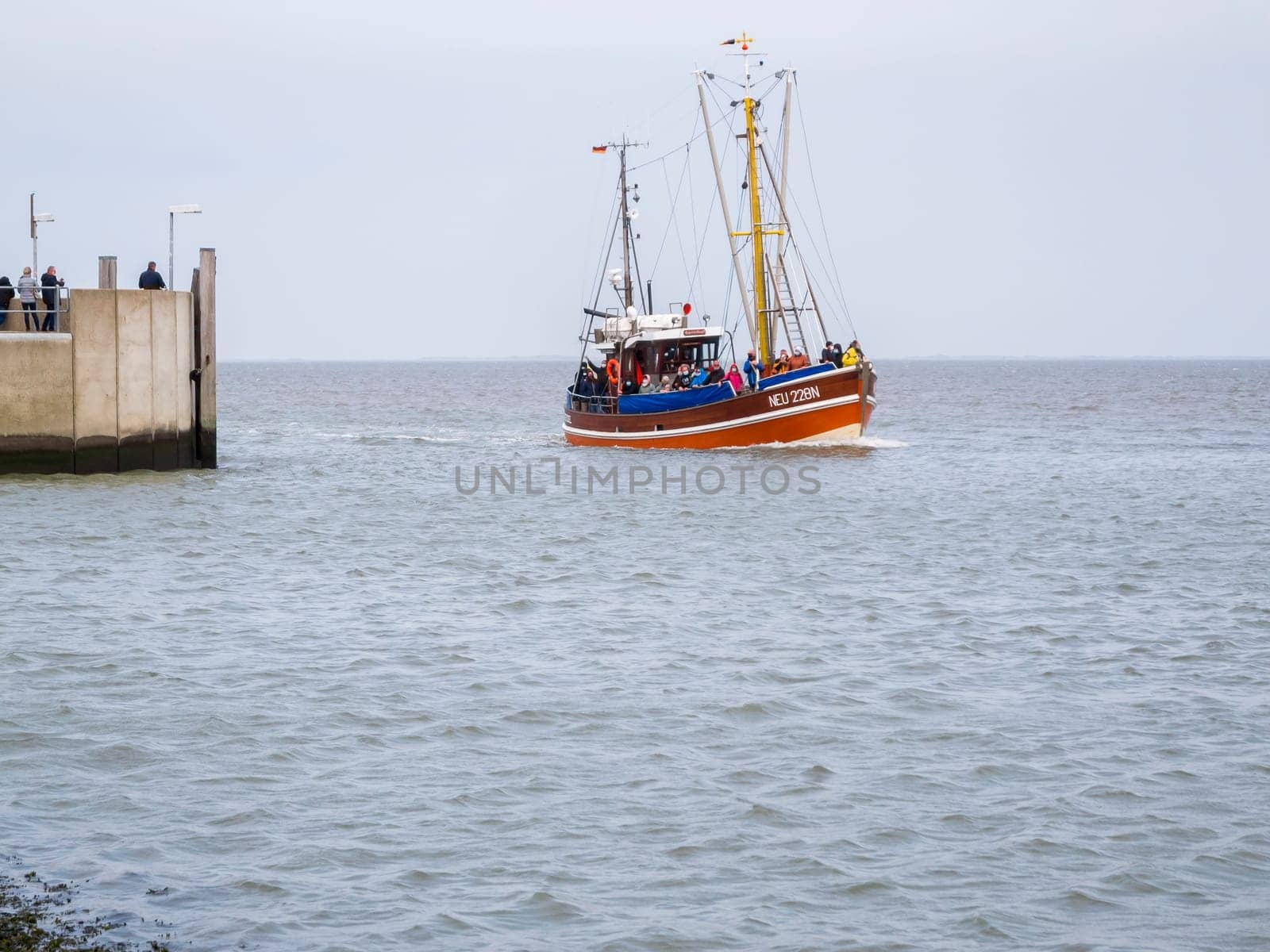 View of the harbor wall at the entrance to Harlesiel in East Freeland with the incoming excursion fishing trawler when the sky is overcast.