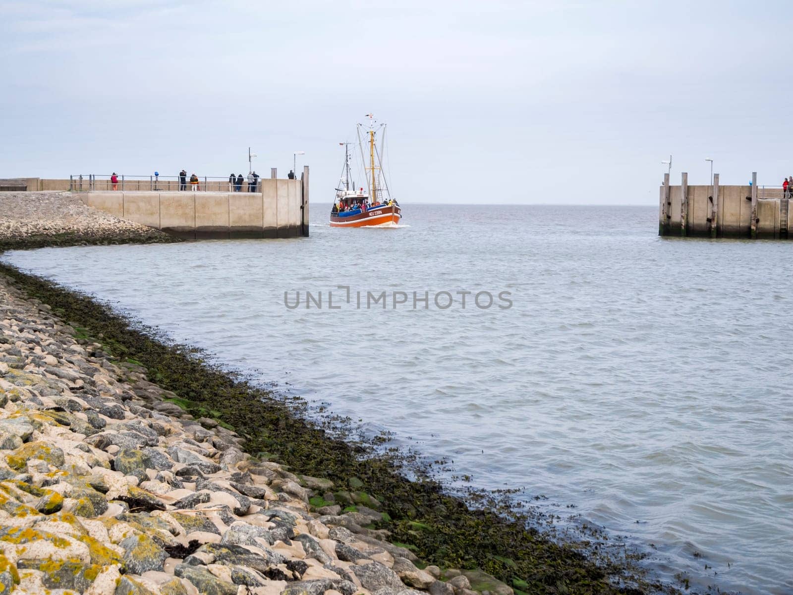 View of the harbor wall at the entrance to Harlesiel in East Freeland with the incoming excursion fishing trawler when the sky is overcast.