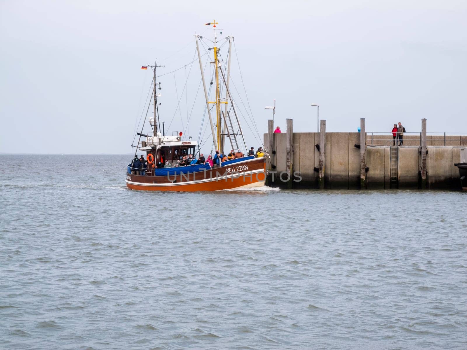 View of the harbor wall at the entrance to Harlesiel in East Freeland with the incoming excursion fishing trawler when the sky is overcast.