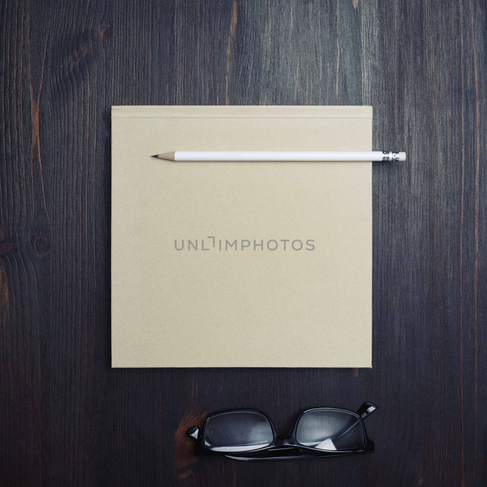 Photo of blank closed brochure, pencil and glasses on wooden background. Responsive design mockup. Stationery elements. Template for placing your design. Top view. Flat lay.