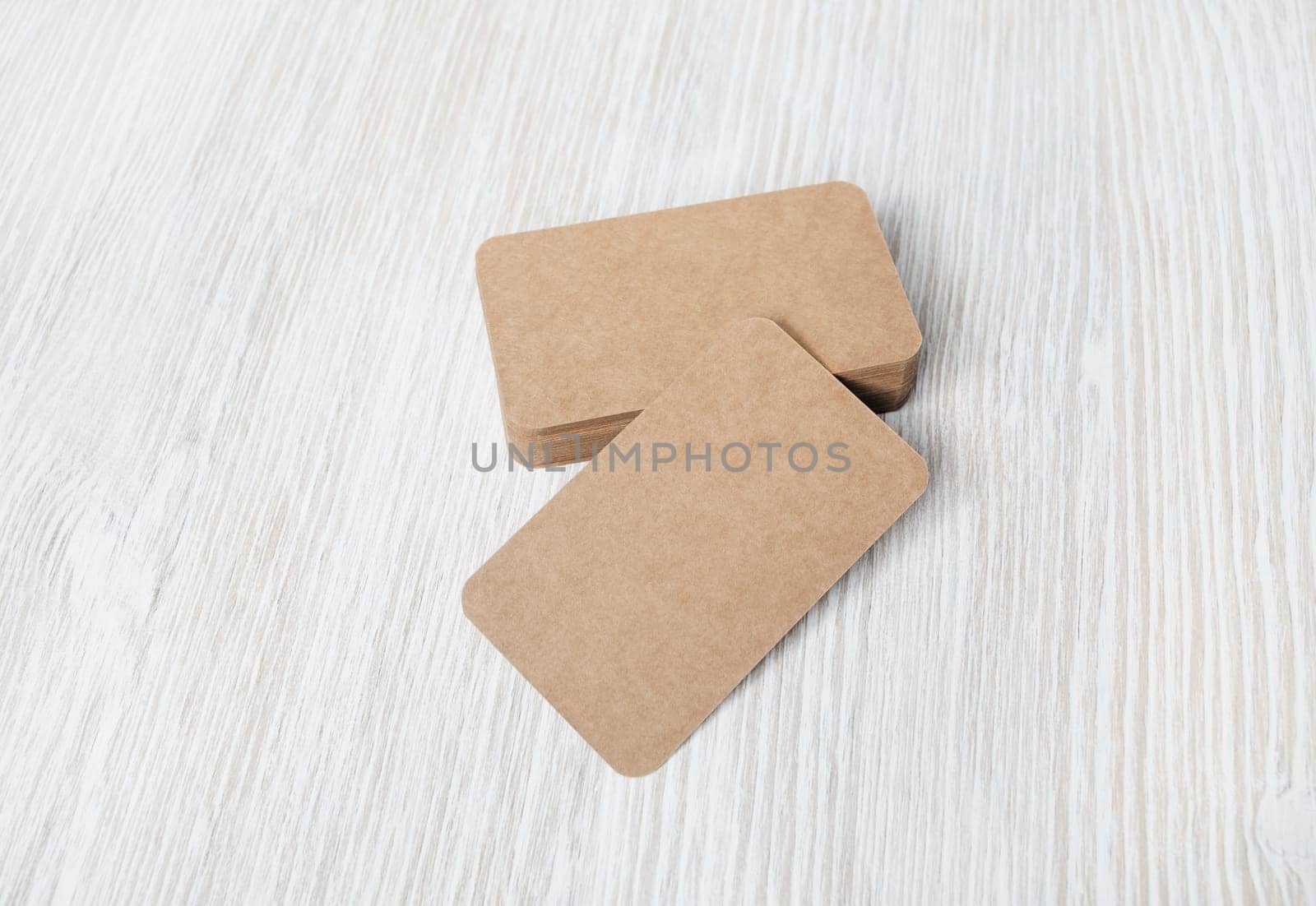 Photo of blank kraft business cards on light wood table background. Template for branding identity.