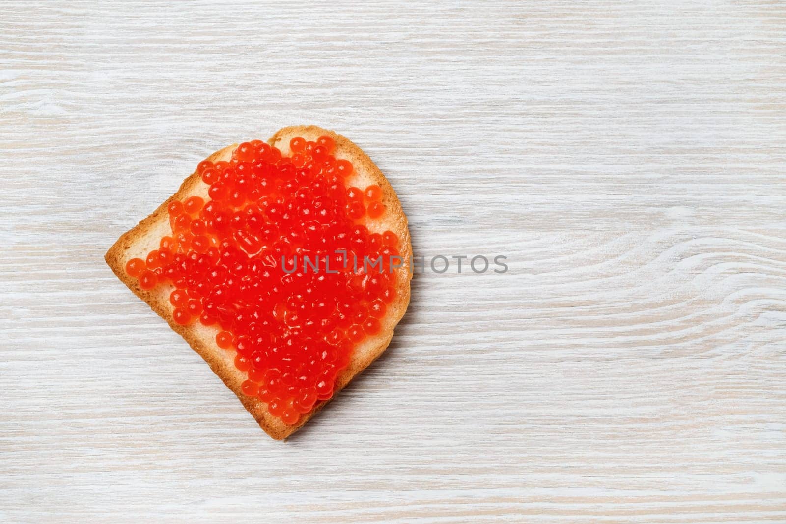 Sandwich with red caviar on light wood table background. Top view. Flat lay.