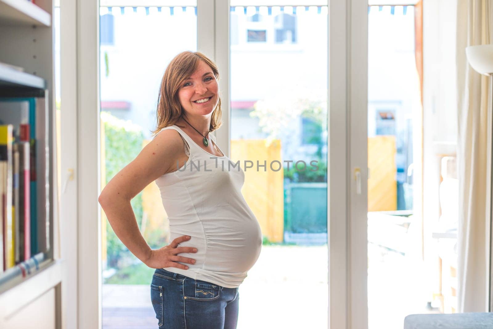 Happy Caucasian pregnant mother touching her tummy, blue jeans, close up