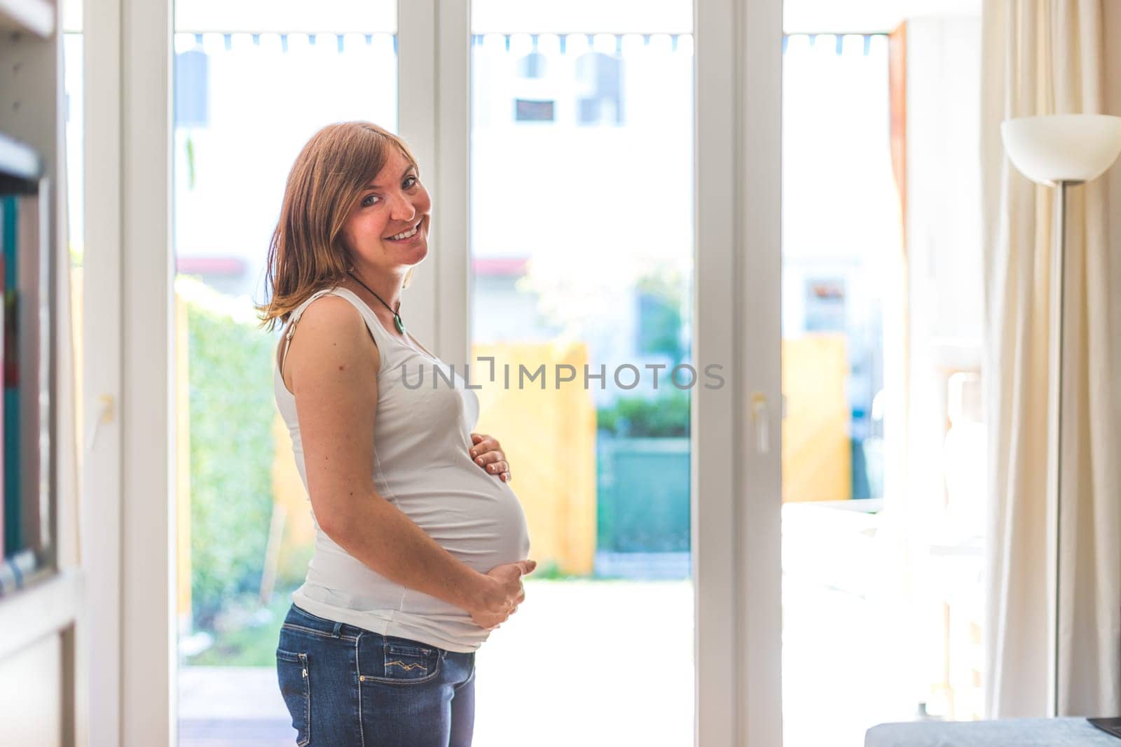 Happy Caucasian pregnant mother touching her tummy, blue jeans, close up