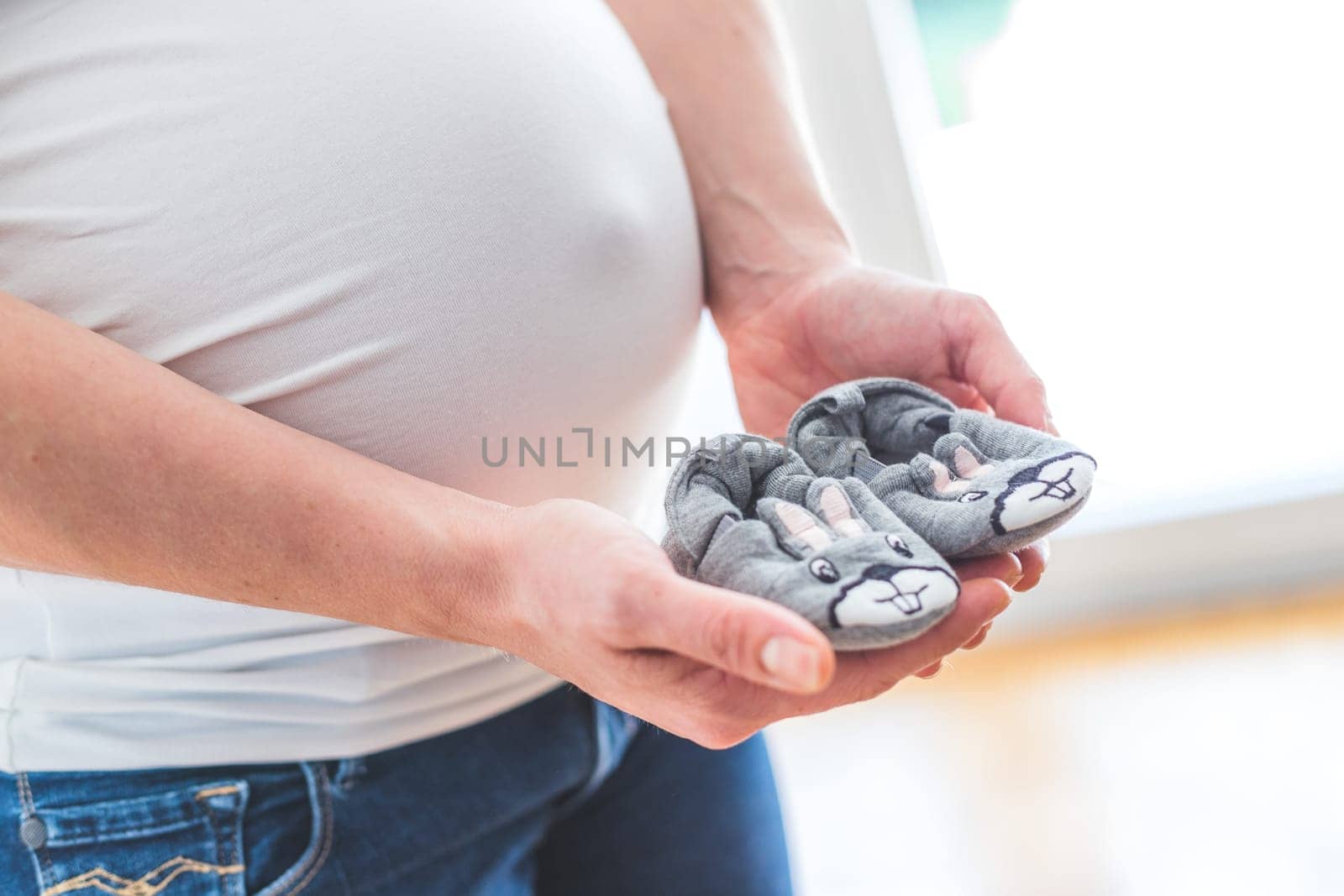 Happy Caucasian pregnant mother holding little baby shoes