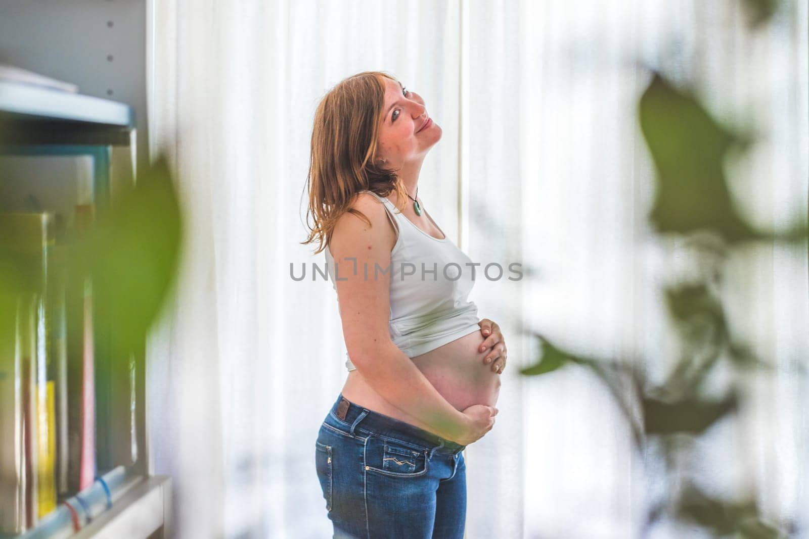 Happy Caucasian pregnant mother touching her naked tummy, blue jeans, close up