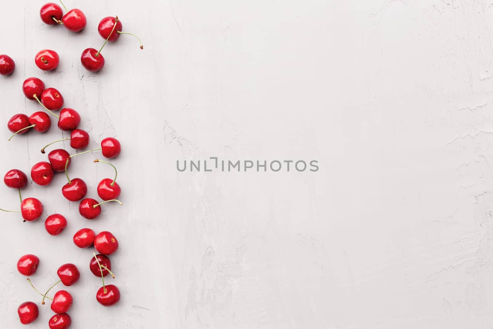 Flat lay top view on gray concrete background with sweet cherry berries and ice cubes. Freshness, summer conceptual minimal background. Eco, bio farm food and fruits concept with copy space area
